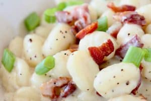 Gnocchi in cream sauce in bowl with crispy bacon bits and diced green onions