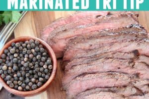 Thinly sliced tri tip on wood cutting board with black peppercorns