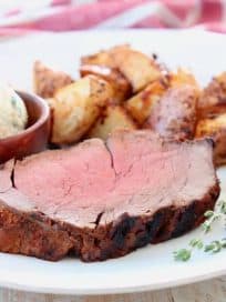 Slice of beef tenderloin on plate with fresh herbs and potatoes