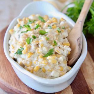 Creamed corn in white oval serving dish with wooden spoon