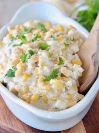 Creamed corn in white oval serving dish with wooden spoon