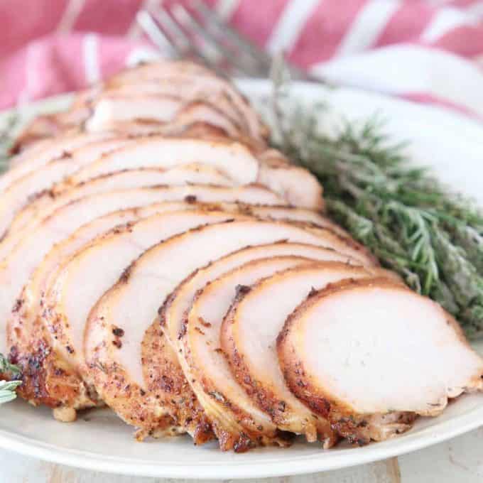 Sliced smoked turkey breast on plate with fresh rosemary and thyme