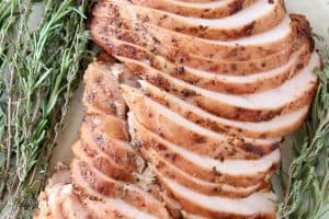 Sliced smoked turkey breast on plate with fresh rosemary and thyme sprigs