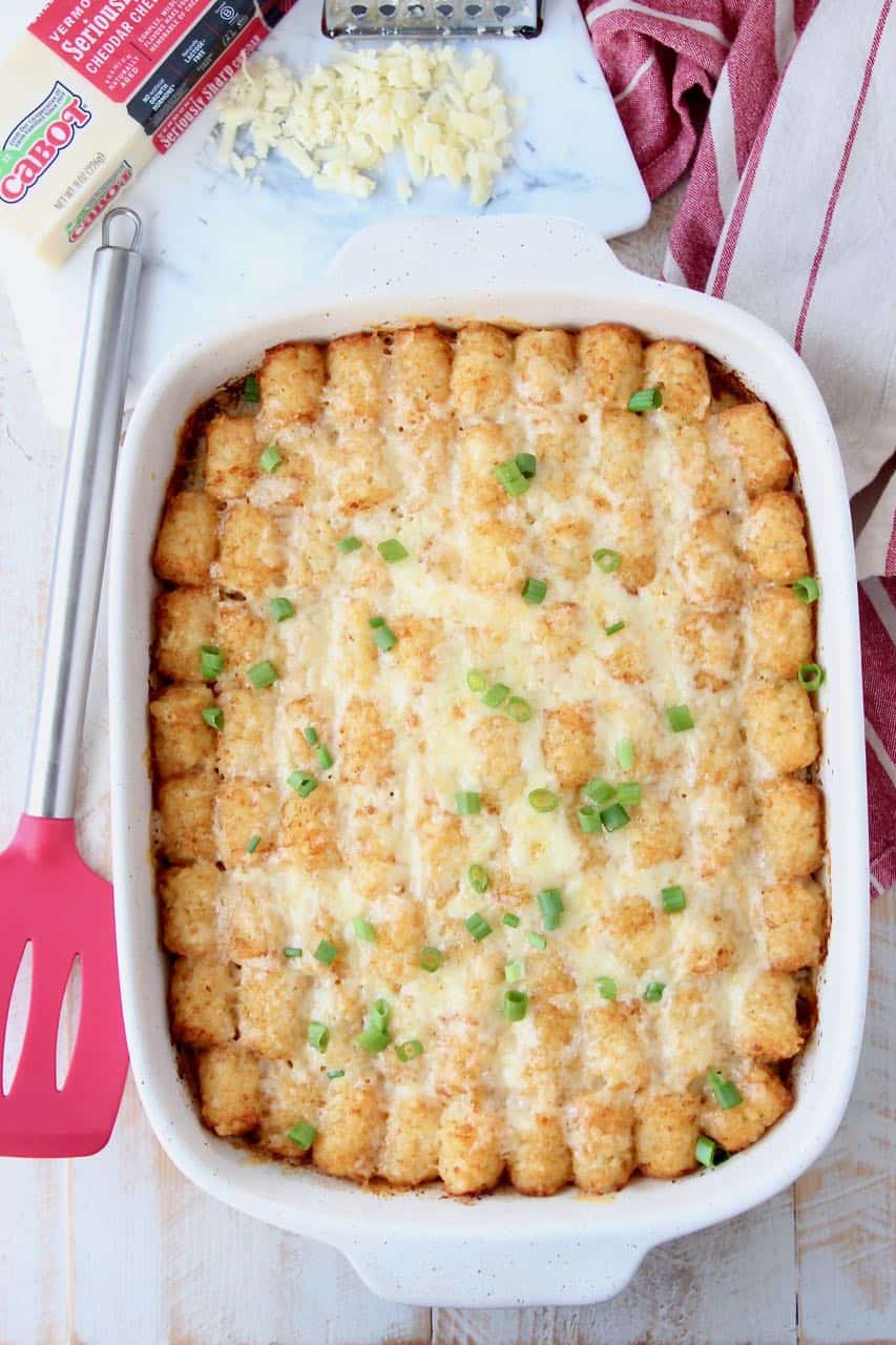 Breakfast tater tot casserole in casserole dish with red spatula on the side