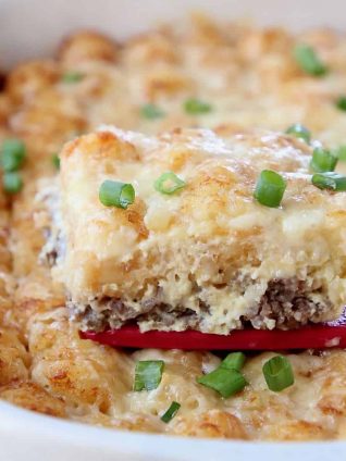 Slice of breakfast tater tot casserole being lifted out of the baking dish with a red spatula