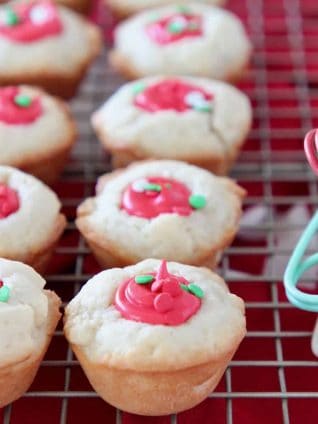 Sugar cookie cups with red frosting filling sitting on wire cooling rack