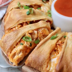 spatula under a piece of buffalo chicken taco ring with a small bowl of buffalo sauce on the side