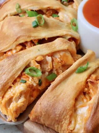 spatula under a piece of buffalo chicken taco ring with a small bowl of buffalo sauce on the side