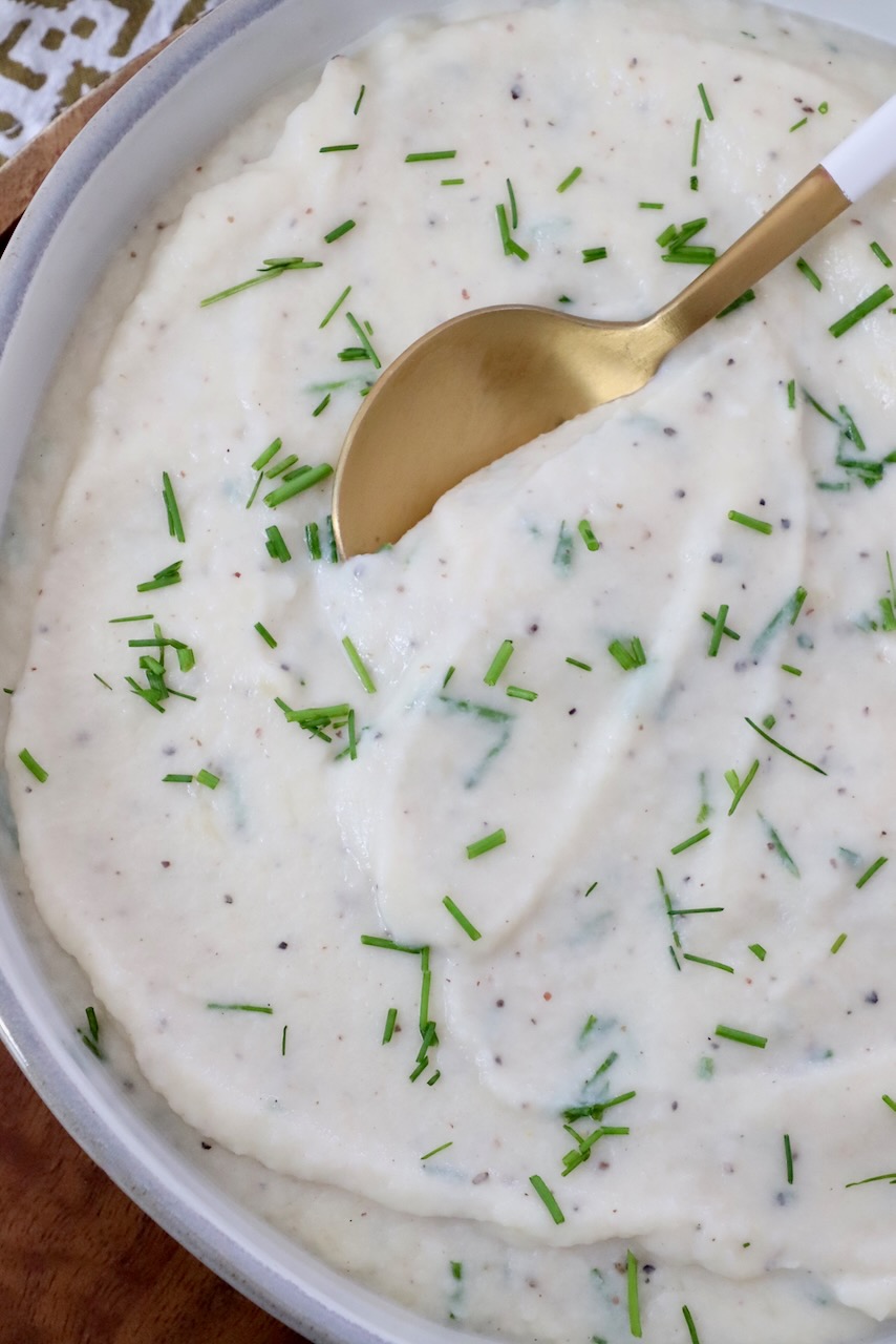 mashed cauliflower in a bowl with chopped chives and a serving spoon