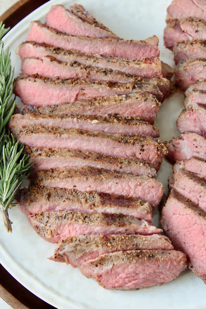 Sliced sous vide tri tip steak on plate with rosemary sprigs