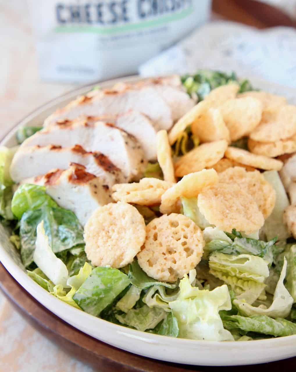 Chicken caesar salad in white bowl topped with parmesan cheese crisps