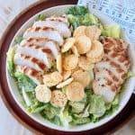 Grilled chicken caesar salad in bowl with parmesan cheese crisps on top