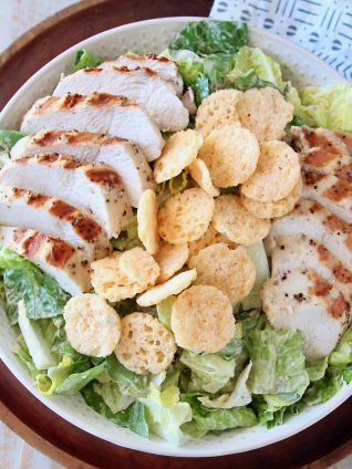 Grilled chicken caesar salad in bowl with parmesan cheese crisps on top