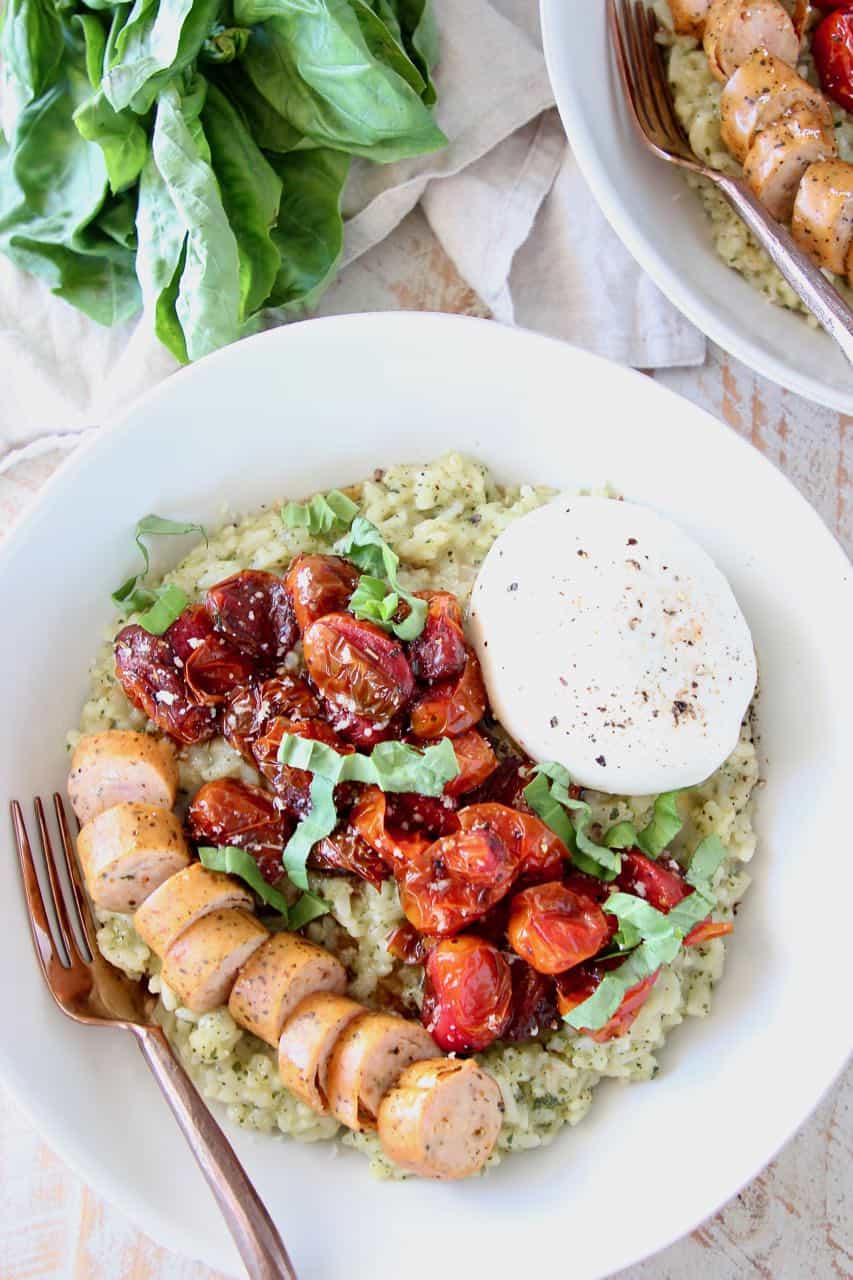 Pesto risotto in bowl, topped with sliced sausage, roasted cherry tomatoes and burrata cheese