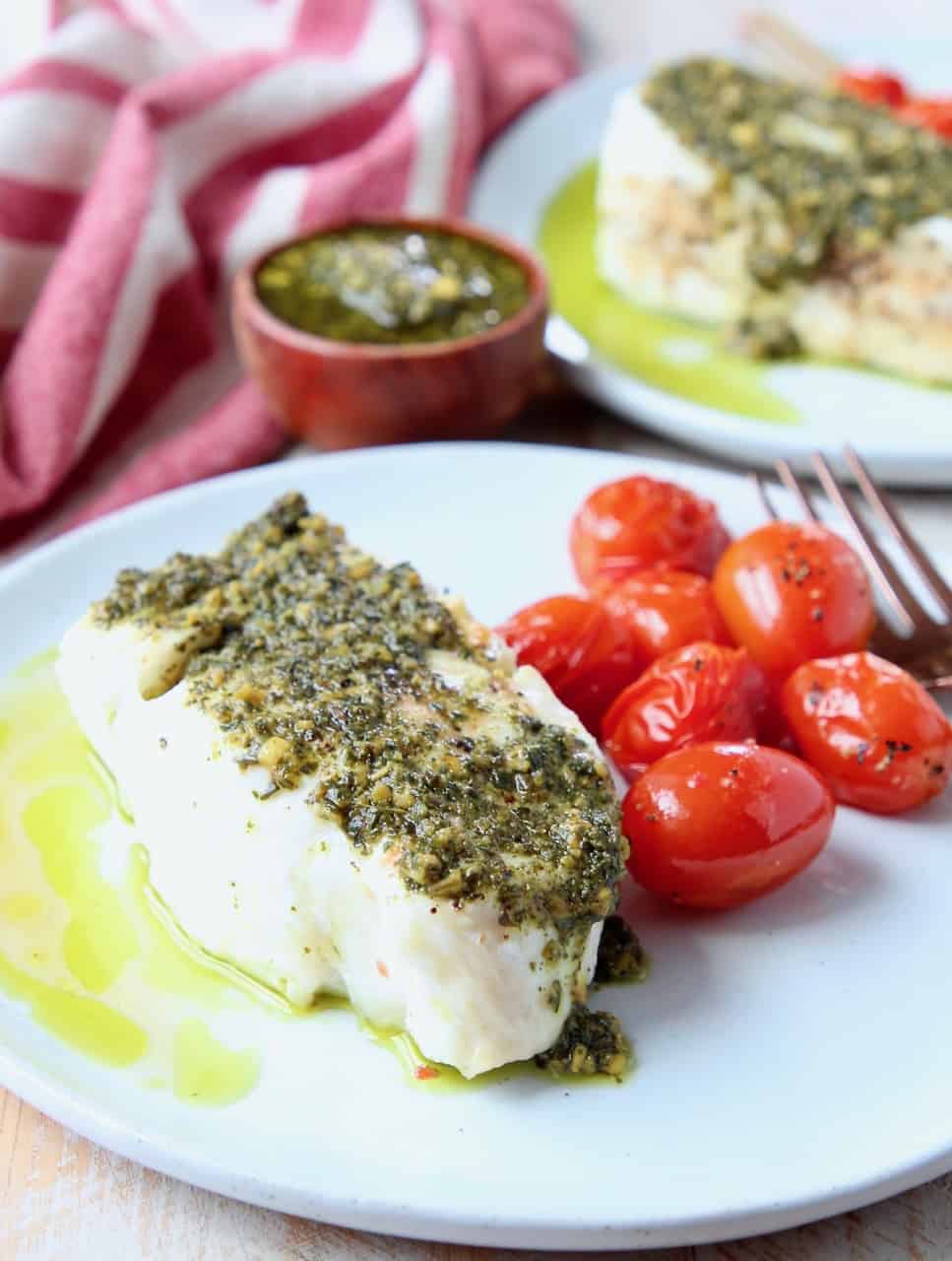 Sea bass topped with pesto on plate with cherry tomatoes