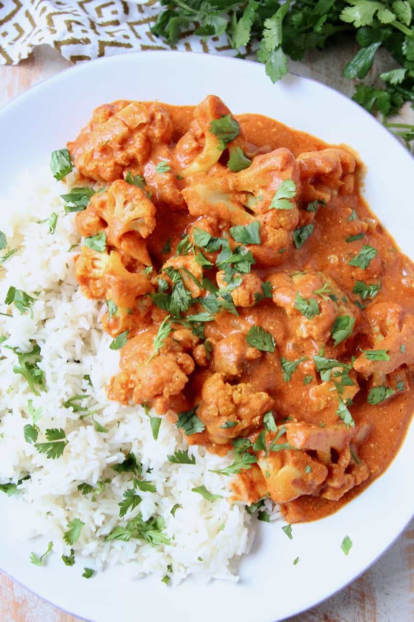 Cauliflower covered in curry sauce on plate with rice and cilantro