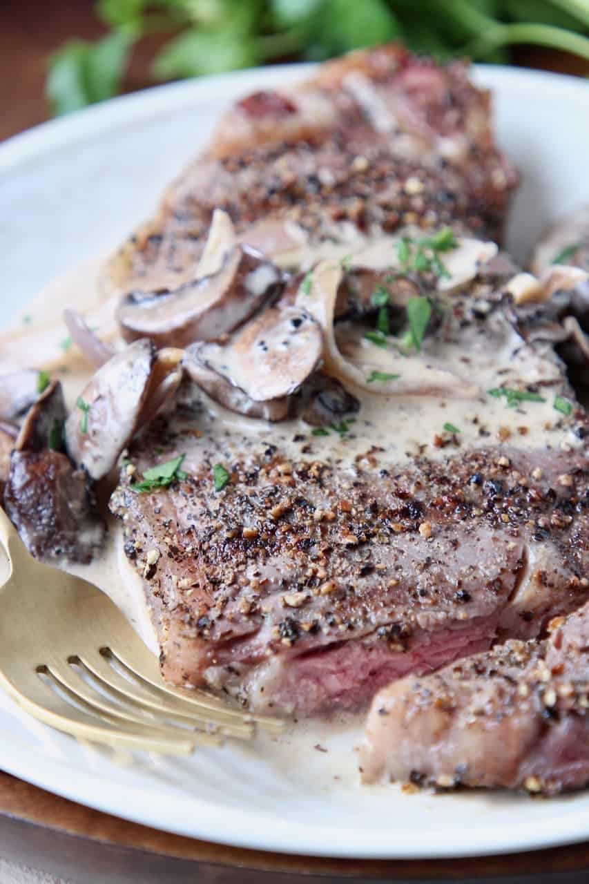 Sliced steak on plate with fork, covered in creamy mushroom sauce