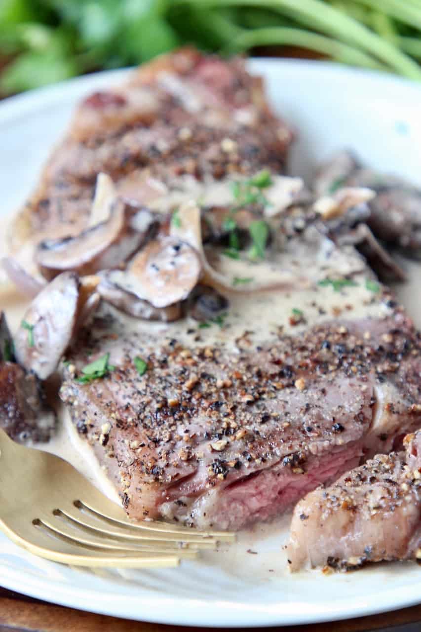 Sliced peppercorn steak on plate with fork and creamy mushroom sauce