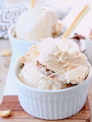 Scoops of peanut butter ice cream in white bowls with gold spoons