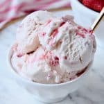 Scoops of strawberry ice cream in white bowl with gold spoon