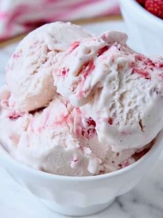 Scoops of strawberry ice cream in white bowl with gold spoon