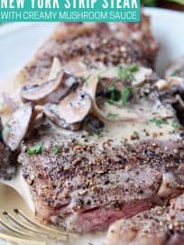 Sliced peppercorn steak on plate with fork and creamy mushroom sauce