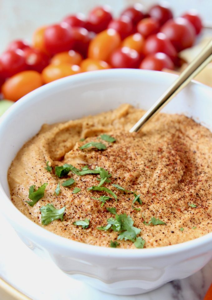 Sriracha hummus in white bowl with gold spoon