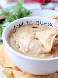 Hand dipping tortilla chip in queso dip
