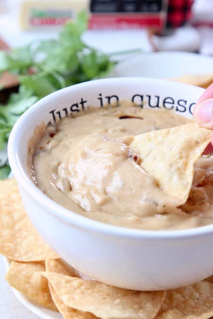 Hand dipping tortilla chip in queso dip
