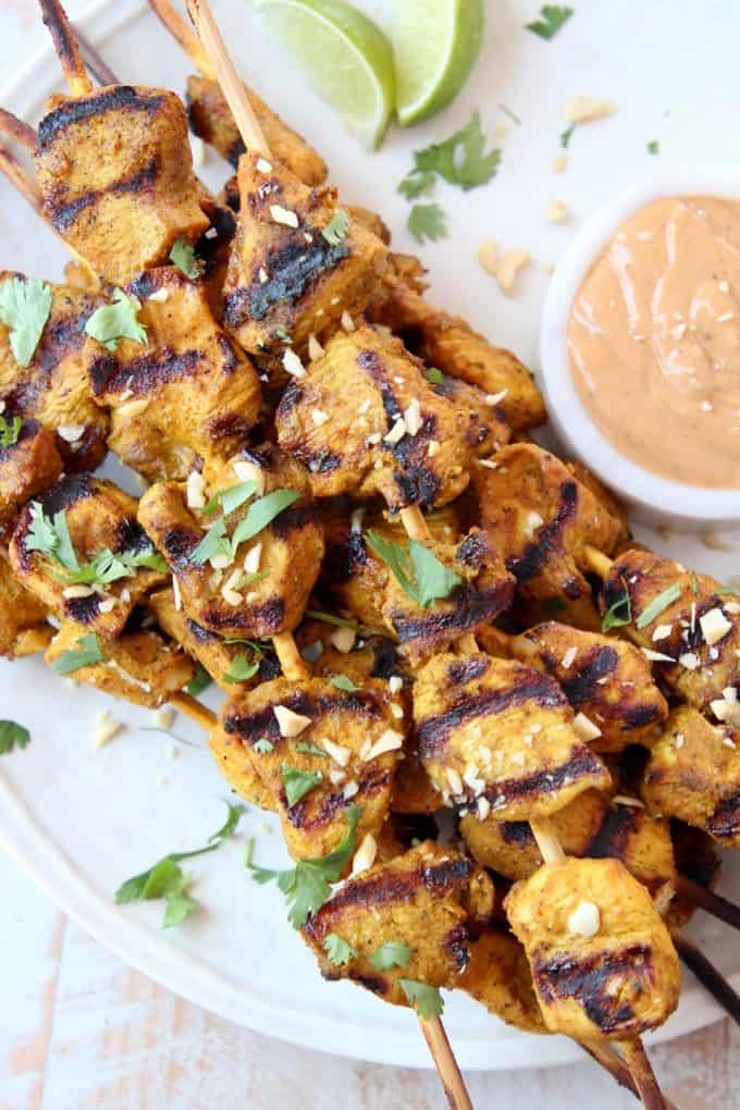 Skewers of chicken on plate with small bowl of peanut sauce