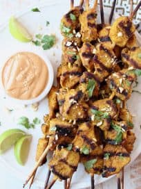 Grilled chicken skewers on plate with bowl of thai peanut sauce