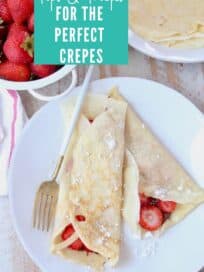 Crepes rolled up on plate filled with nutella and sliced strawberries