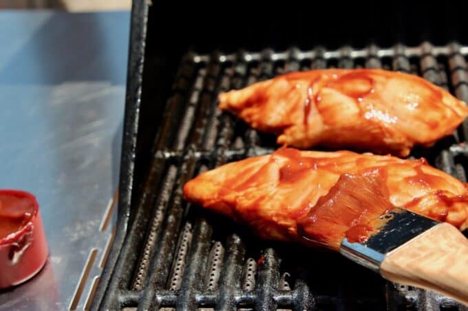 brushing bbq sauce on chicken on grill