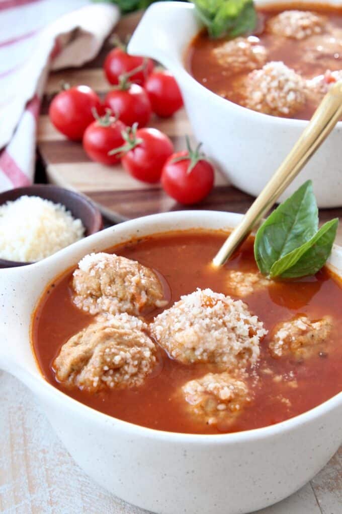 Meatball soup in bowl with basil leaves on the side