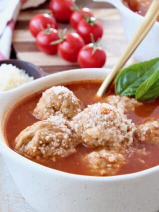 Meatball soup in bowl with gold spoon and fresh basil leaves