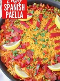 Overhead image of paella in skillet topped with sliced peppers and lemon wedges