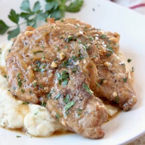 two pork chops on plate covered with gravy, on top of mashed potatoes