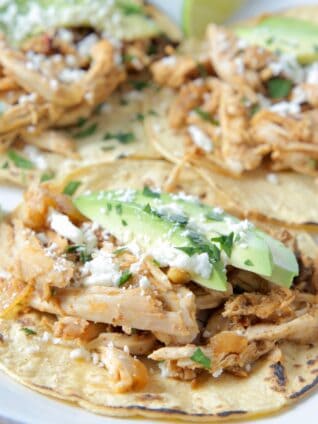 shredded chicken tacos on plate topped with sliced avocado