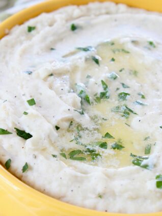 mashed potatoes topped with melted butter and chopped parsley in yellow bowl