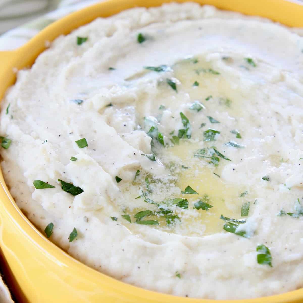 mashed potatoes topped with melted butter and chopped parsley in yellow bowl