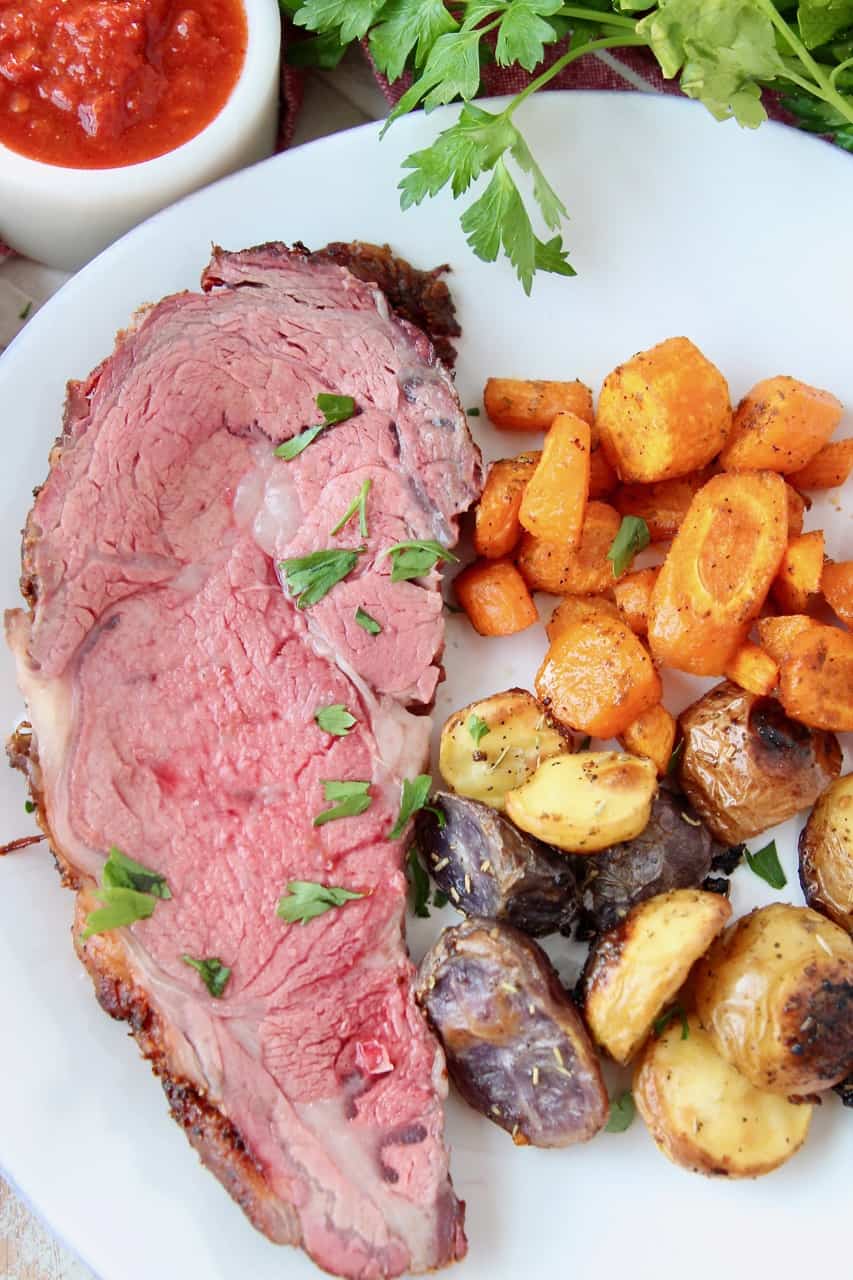 overhead image of sliced prime rib on plate with roasted vegetables