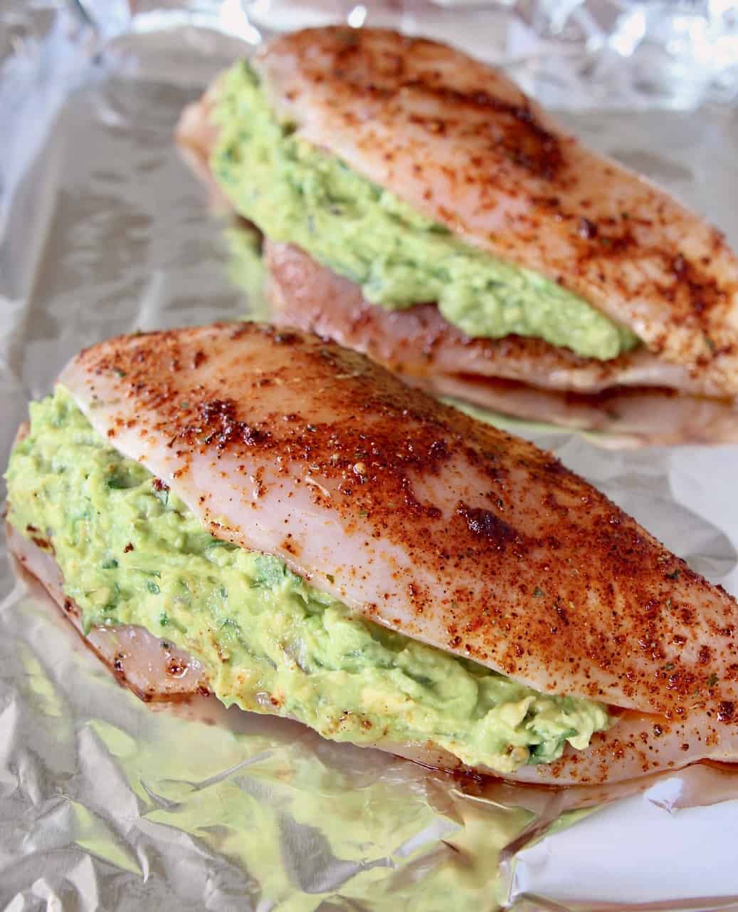 Uncooked guacamole stuffed chicken on foil-lined baking sheet