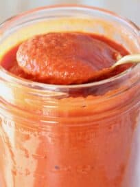 spoon of enchilada sauce lifted out of mason jar of sauce