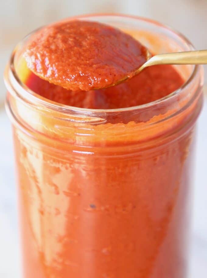 spoon of enchilada sauce lifted out of mason jar of sauce
