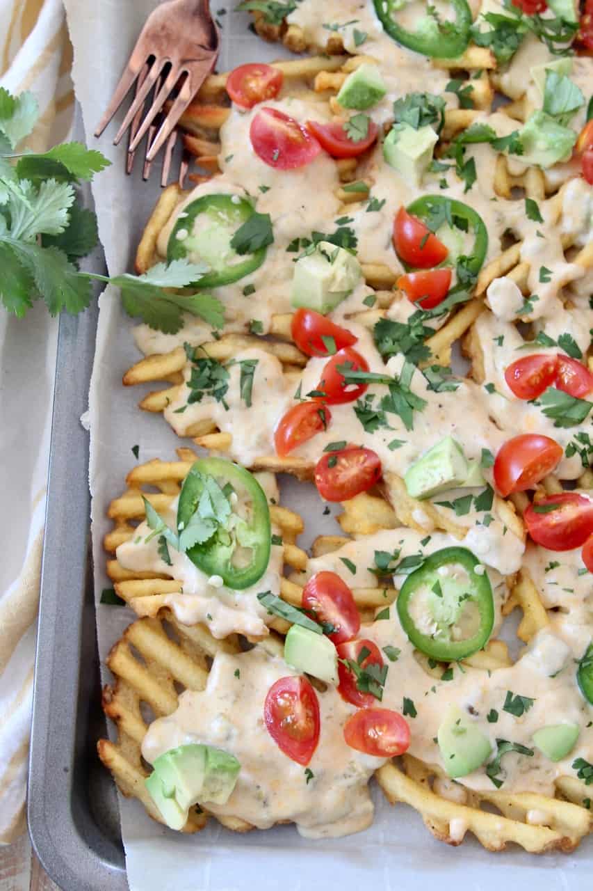 overhead image of waffle fries on baking sheet covered in cheese sauce