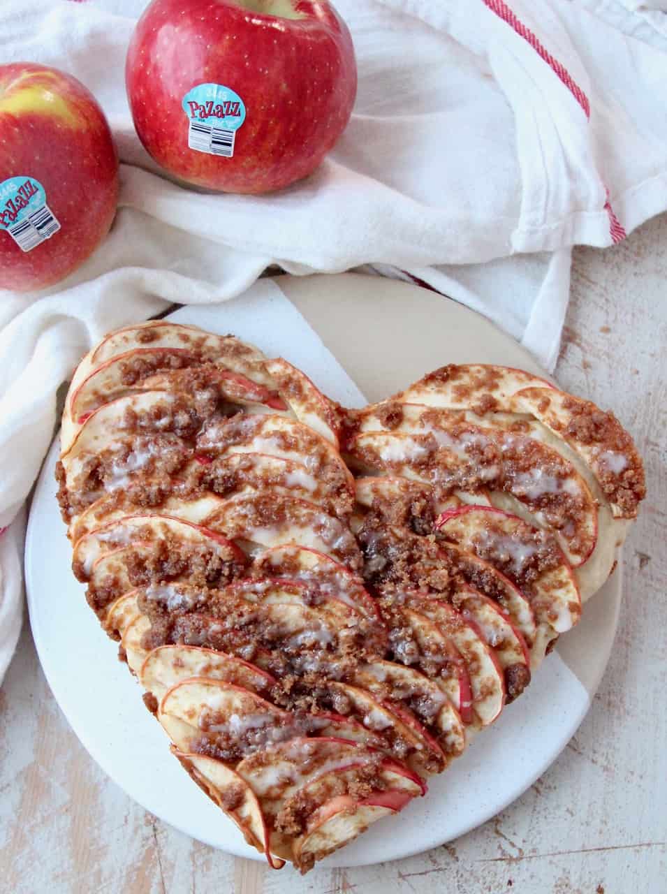 overhead image of heart shaped apple pizza on serving dish with fresh apples on the side