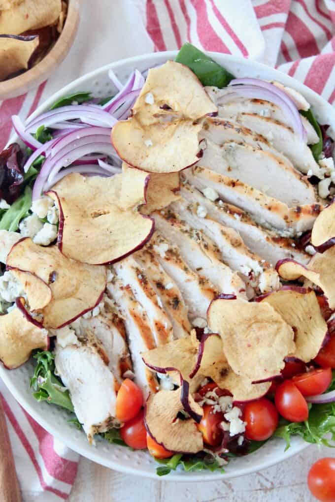 sliced chicken on top of salad in bowl with apple chips