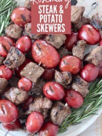 grilled cubes of sirloin on skewers with red potatoes stacked up on a plate with rosemary sprigs