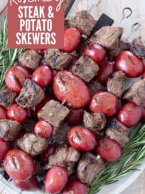 grilled cubes of sirloin on skewers with red potatoes stacked up on a plate with rosemary sprigs