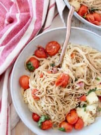 cooked angel hair pasta in bowl with cherry tomatoes, basil and mozzarella cheese